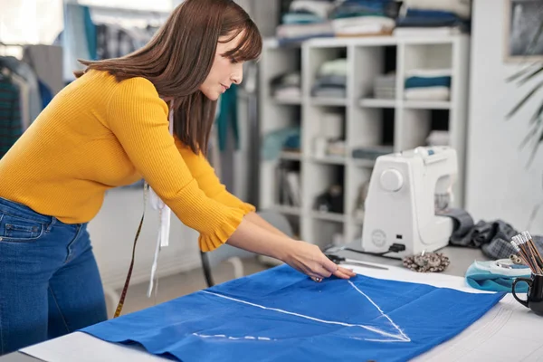 Criativa designer de moda caucasiano de pé em seu estúdio e esquema de desenho em linho azul para um belo vestido de noite . — Fotografia de Stock