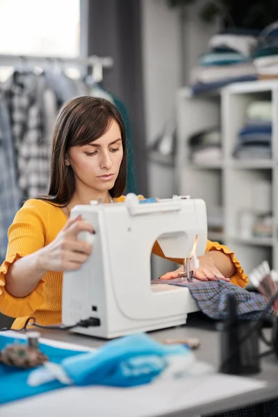 Focused charming caucasian fashion designer sitting in her studio and sewing beautiful evening dress. — Stock Photo, Image