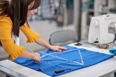 Yaratıcı Kafkas moda tasarımcısı stüdyosunda duruyor ve güzel bir gece elbisesi için mavi kumaş üzerine çizimler yapıyor..