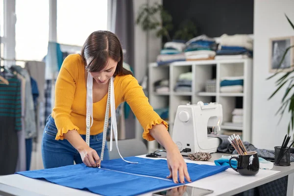 Diseñador de moda caucásica creativa de pie en su estudio y esquema de dibujo en tela azul para un hermoso vestido de noche . —  Fotos de Stock