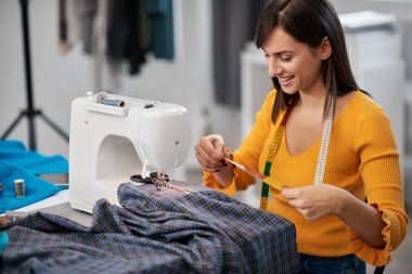 Stüdyosunda oturan beyaz tenli moda tasarımcısı güzel bir gece elbisesi için tekstil ölçüyor..