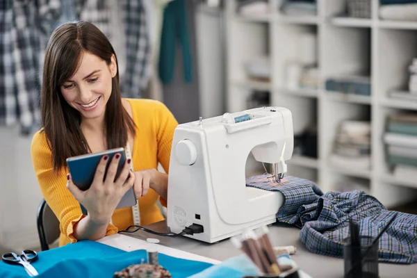 Smiling positive caucasian brunette sitting in her fashion studio and using tablet. — Stock Photo, Image