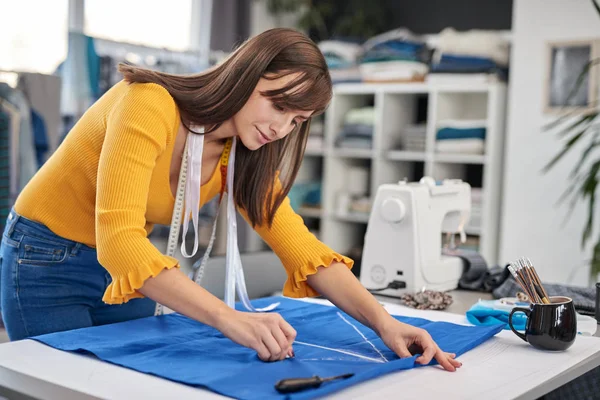 Criativa designer de moda caucasiano de pé em seu estúdio e esquema de desenho em linho azul para um belo vestido de noite . — Fotografia de Stock