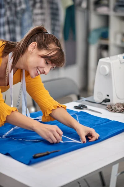 Diseñador de moda caucásica creativa de pie en su estudio y esquema de dibujo en lino azul para un hermoso vestido de noche . — Foto de Stock