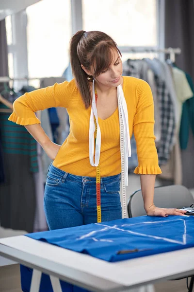 Bonita criativa designer de moda caucasiana de pé em seu estúdio e olhando para têxteis . — Fotografia de Stock