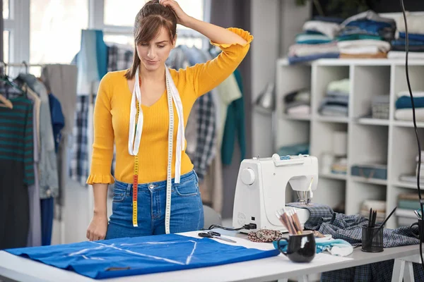 Hermosa creativa diseñadora de moda caucásica de pie en su estudio y mirando el textil . —  Fotos de Stock