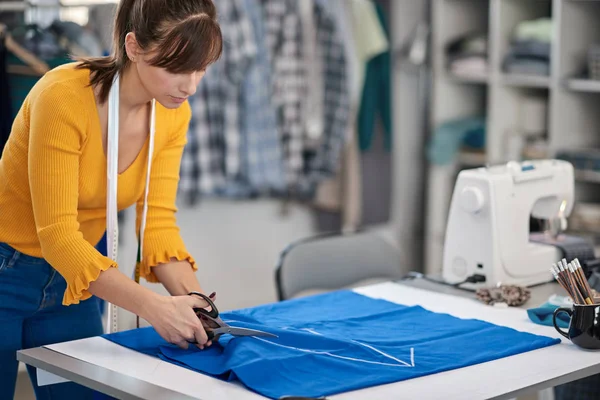 Costureira dedicada em pé ao lado da mesa e corte de têxteis para vestido elegante . — Fotografia de Stock