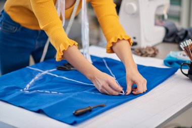 Yaratıcı Kafkas moda tasarımcısı stüdyosunda duruyor ve güzel bir gece elbisesi için mavi keten üzerine çizimler yapıyor..