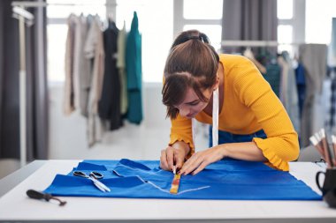 Yaratıcı Kafkas moda tasarımcısı stüdyosunda duruyor ve güzel bir gece elbisesi için mavi keten üzerine çizimler yapıyor..