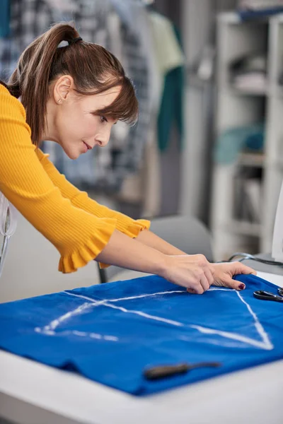 Creative caucasian fashion designer standing in her studio and dCreative caucasian fashion designer standing in her studio and drawing scheme on blue linen for a beautiful night dress. — 스톡 사진