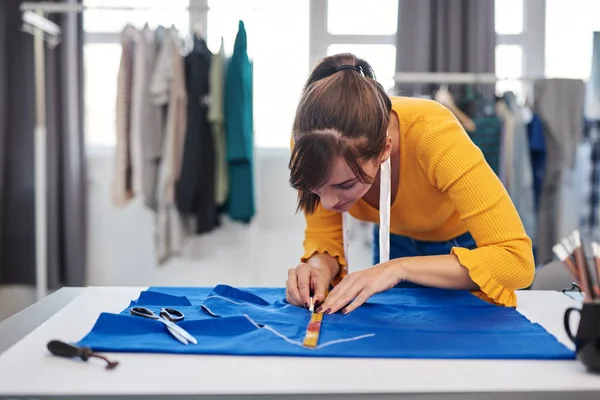 Diseñador de moda caucásica creativa de pie en su estudio y esquema de dibujo en lino azul para un hermoso vestido de noche . —  Fotos de Stock