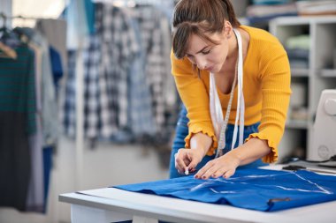 Yaratıcı Kafkas moda tasarımcısı stüdyosunda duruyor ve güzel bir gece elbisesi için mavi keten üzerine çizimler yapıyor..