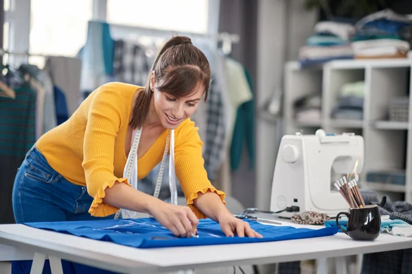 Creative caucasian fashion designer standing in her studio and drawing scheme on blue linen for a beautiful evening dress.g in her studio and d — Stock Photo, Image