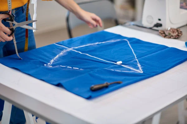 Costureira dedicada em pé ao lado da mesa e corte de têxteis para vestido elegante . — Fotografia de Stock