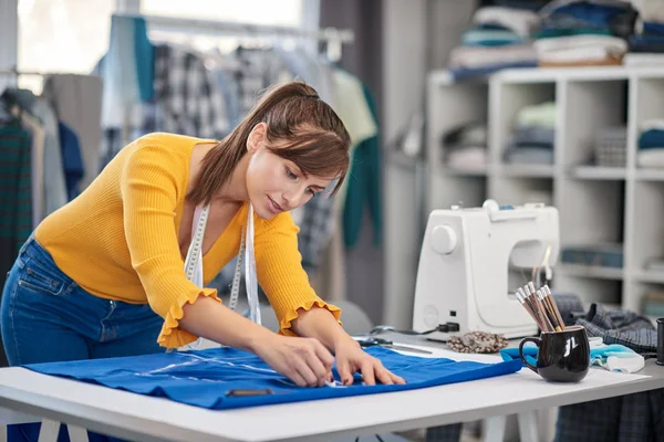 Kreative kaukasische Modedesignerin steht in ihrem Atelier und zeichnet Schema auf blauem Leinen für ein schönes Abendkleid. — Stockfoto