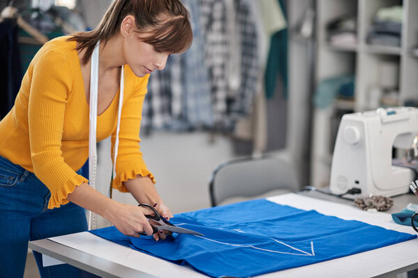 Посвящается швея стоя рядом со столом и резки текстиля для элегантного платья
.