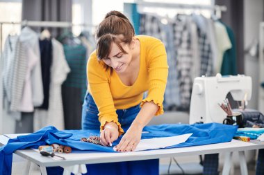 Yaratıcı Kafkas moda tasarımcısı stüdyosunda duruyor ve güzel bir gece elbisesi için mavi keten üzerine çizimler yapıyor..