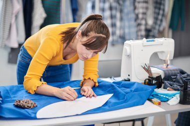 Yaratıcı Kafkas moda tasarımcısı stüdyosunda duruyor ve güzel bir gece elbisesi için mavi keten üzerine çizimler yapıyor..