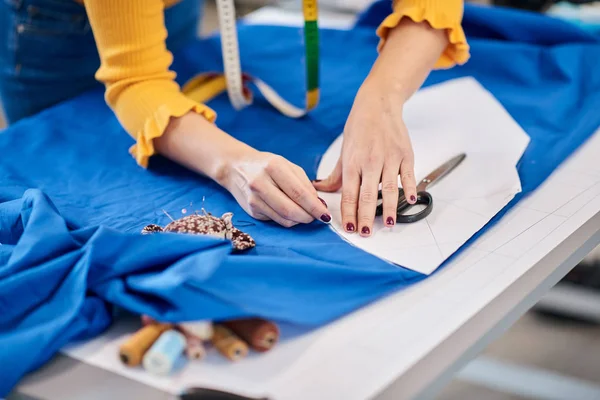 Diseñador de moda caucásica creativa de pie en su estudio y esquema de dibujo en lino azul para un hermoso vestido de noche . — Foto de Stock