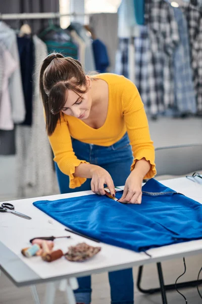 Ung kreativ kaukasisk sömmerska som står i sin studio och mäter kjol med måttband. — Stockfoto