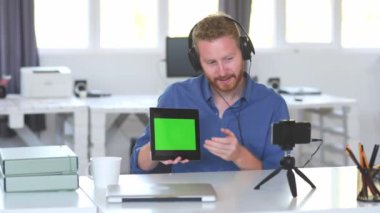 Yakışıklı Kafkas çalışanı internet üzerinden sunum yapıyor. Ellerde tablet ve baş kulaklıkvardır. İş konseptini başlatın.