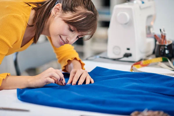 Charming caucasian smiling dedicated seamstress drawing  seam with chalk on a skirt. — Stock Photo, Image