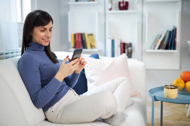 Güzel evindeki kanepede oturan genç, çekici esmer kız ve mesaj yazıyor..