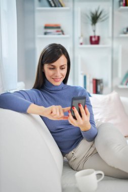 Güzel evindeki kanepede oturan genç, çekici esmer kız ve mesaj yazıyor..