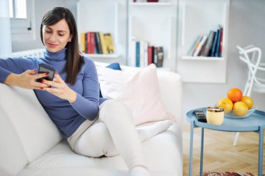 Genç, çekici esmer, güzel evinde kanepede oturuyor ve mesaj yazıyor..