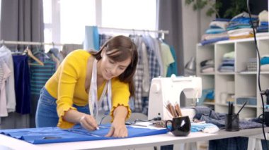 Yaratıcı Kafkas moda tasarımcısı stüdyosunda duruyor ve güzel bir gece elbisesi için mavi keten üzerine çizimler yapıyor..