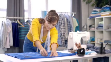 Yaratıcı Kafkas moda tasarımcısı stüdyosunda duruyor ve güzel bir gece elbisesi için mavi keten üzerine çizimler yapıyor..