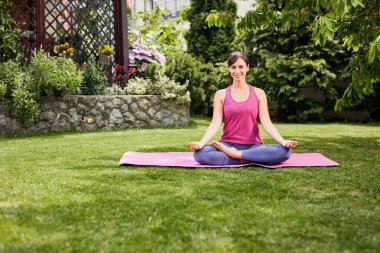 Genç, çekici esmer, arka bahçesinde oturuyor, Lotus pozisyonunda ve meditasyon yapıyor..