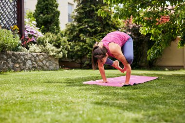 Genç, çekici, güçlü, esnek, yoga pozisyonu almış, ellerinin üzerinde duran bir Yogi kadını. Arka bahçe dış tarafı..
