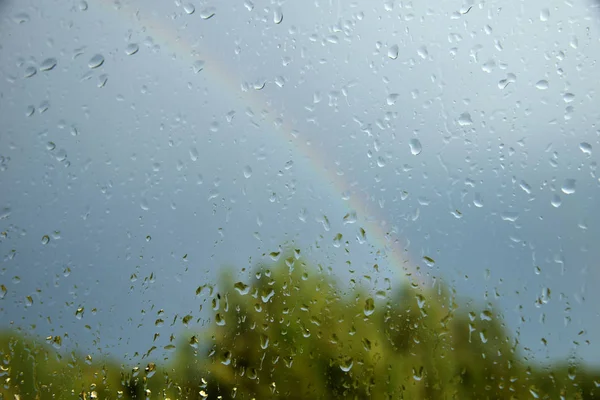 View of forest and rainbow through window with drops