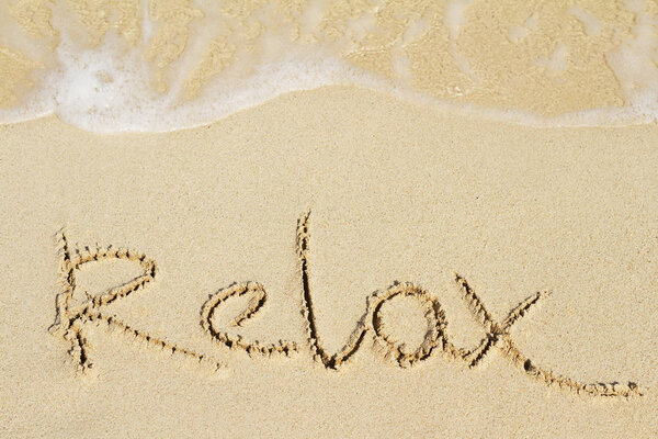 Word Relax is hand written on sand of beach