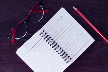 Kırmızı gözlükler, not defteri ve kalem.