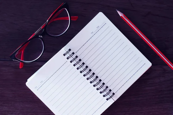Kırmızı gözlükler, not defteri ve kalem.