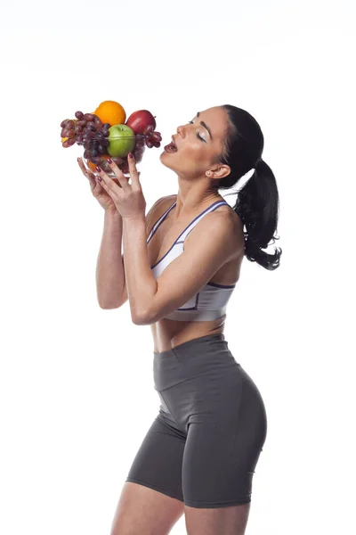 Mulher Morena Sexy Terno Fitness Comendo Frutas Estúdio Tiro Isolado — Fotografia de Stock