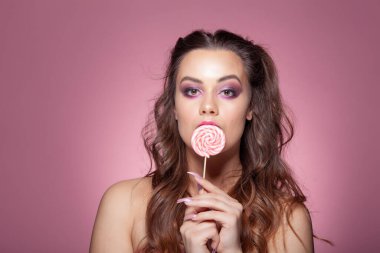Genç seksi kadın lolipop yiyor. Pembe arka planda stüdyo çekimi.