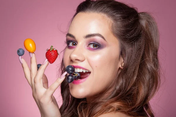 年轻性感的女人吃她手指上的水果 粉红背景的工作室拍摄 — 图库照片