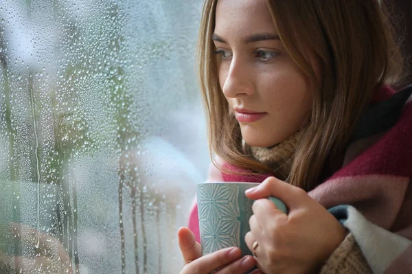 Chica con una taza de bebida caliente en frente de una ventana — Foto de Stock