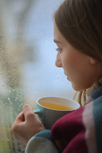Chica con una taza de bebida caliente en frente de una ventana — Foto de Stock