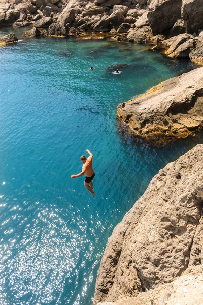 Un uomo che vola da una roccia nell'acqua . — Foto Stock