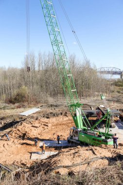 İnşaat alanındaki vincin yanındaki işçiler. Volkhov Nehri üzerinde bir motor köprüsü inşa edilmeye başlandı.