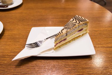 Kahve barında servis edilen tepsi ve çatalla bir dilim badem ezmeli kek.