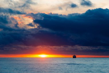 Gün batımı manzarası bulutlu güneş yansıması ve ufukta gemi var.