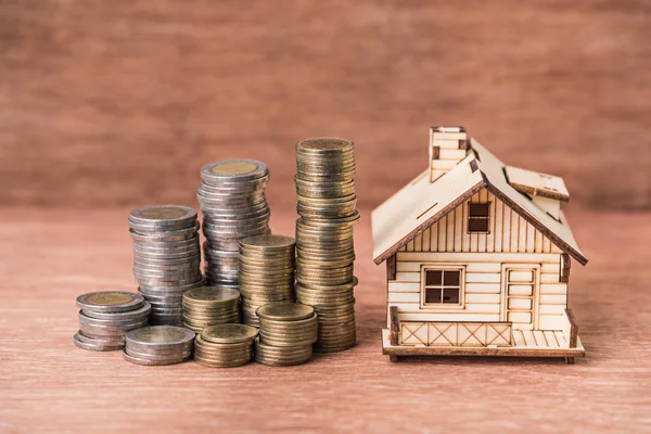 Munt stack en huis model op bruin houten achtergrond — Stockfoto