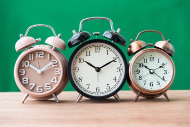 yeşil arka plana sahip ahşap masa üç çalar saat