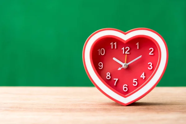 Red heart alarm clock on wooden table with green background — Stock Photo, Image