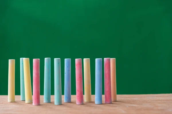 Krijtjes in een verscheidenheid van kleuren op tafel met groene achtergrond — Stockfoto